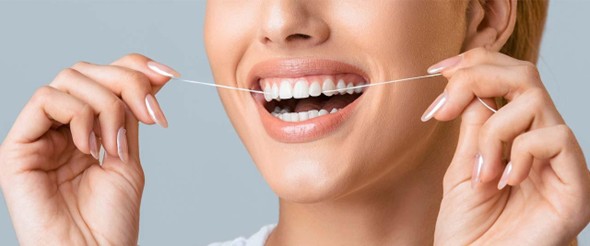 Mujer sonriendo mientras usa hilo dental, un hábito clave para prevenir enfermedades bucales y entender qué es la gingivitis